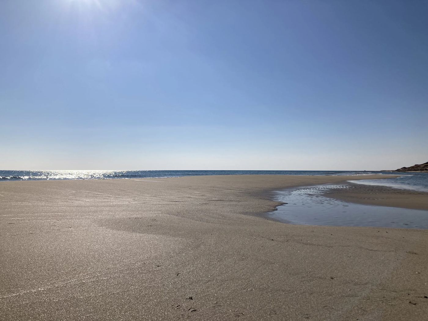 A wide beach at low tide, the sea drawing back under a pale sky